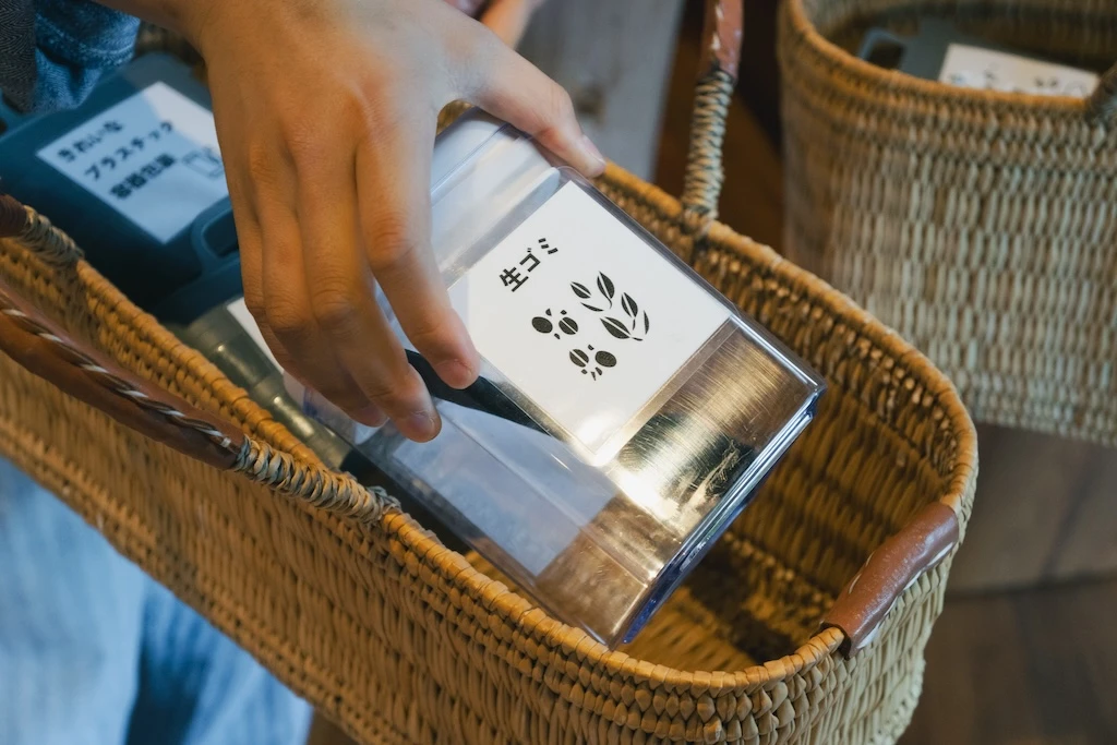 A photograph of a basket containing a small garbage can. He is holding a clear cased trash can labeled “Food Waste.”