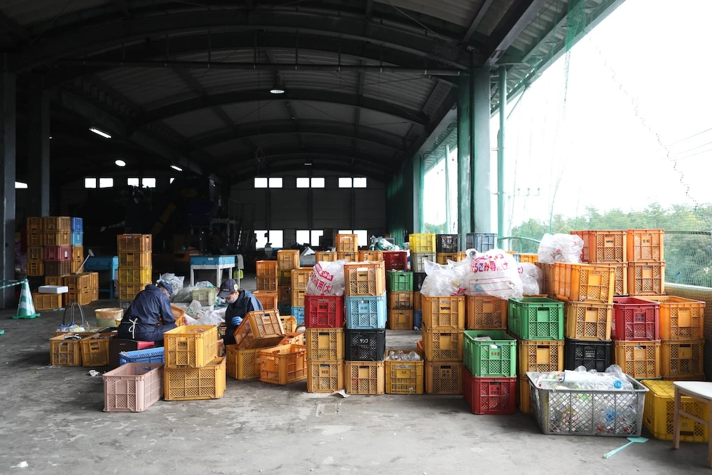 Photo of a pull at a trash station in Osaki Town. Two staff members are working among countless piles of cases.