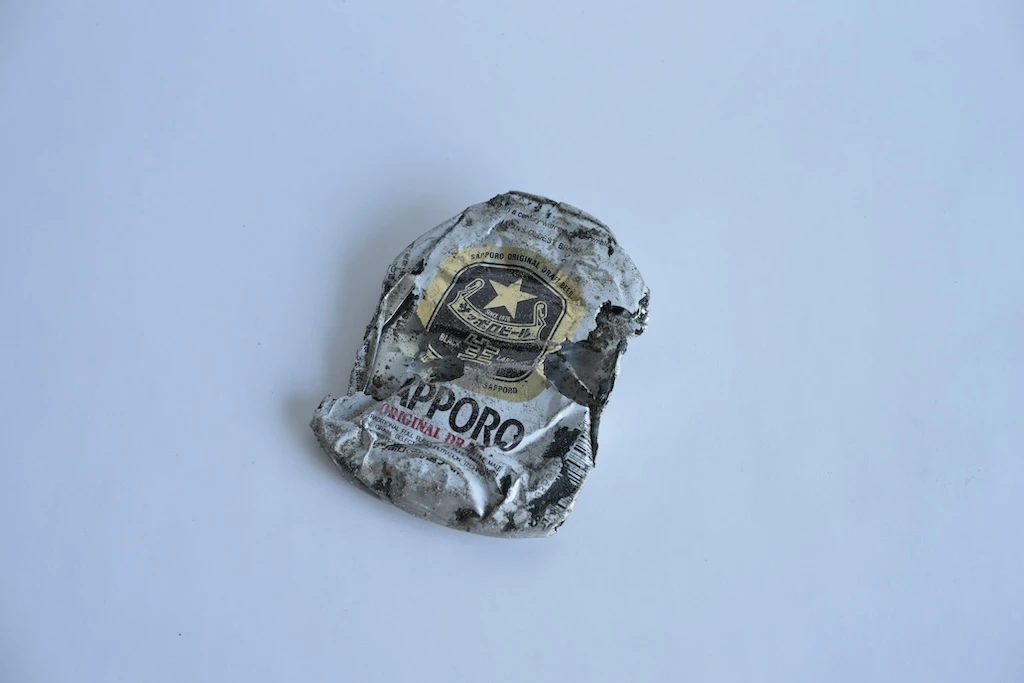 Picture of a flattened and crushed can of beer. The whole thing is dirty, deteriorated and has holes in it.