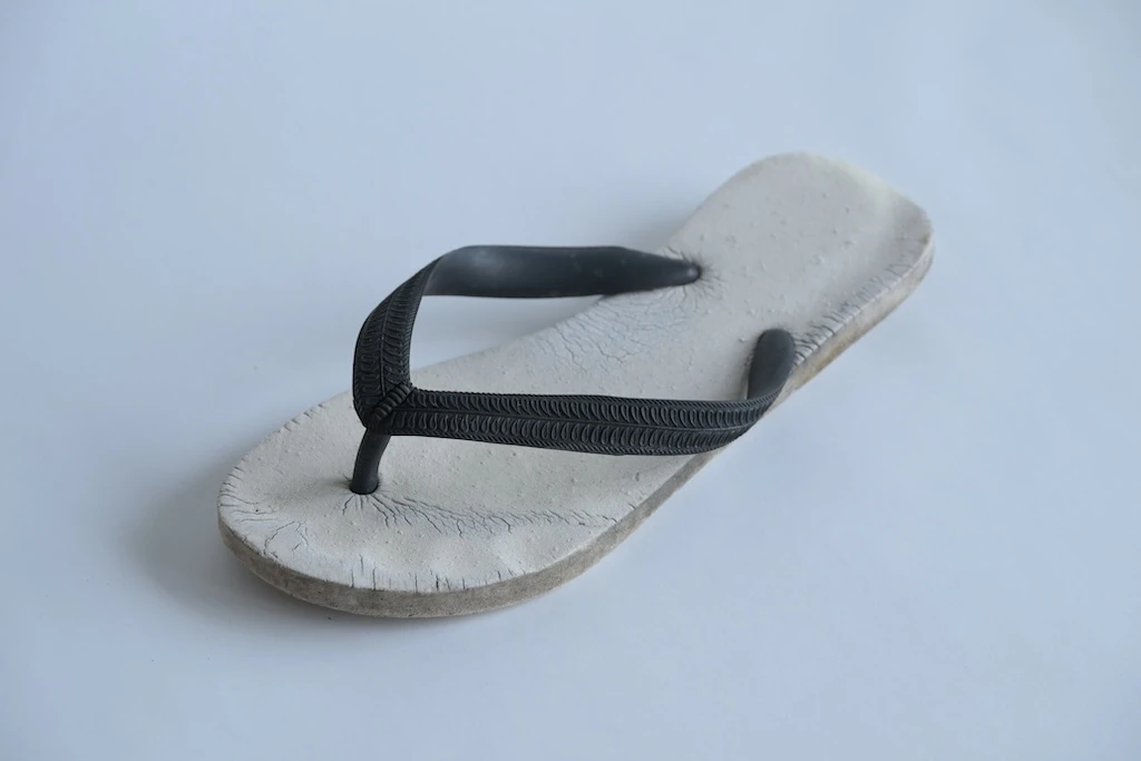 Photo of one of the sandals. The body appears to be made of white leather and is cracked throughout. The tongue portion is black.