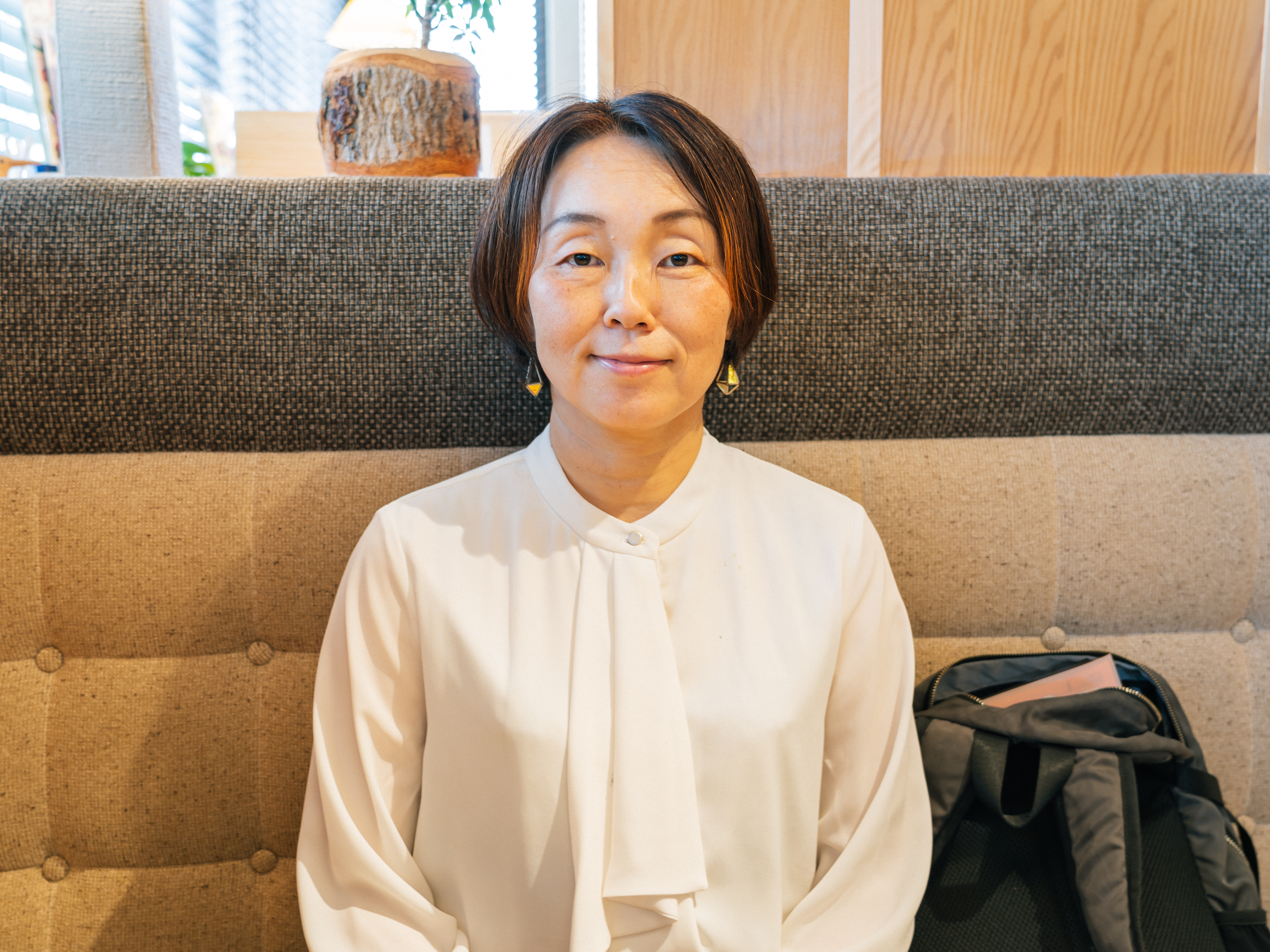 ショートボブヘアで、白いブラウスを着た女性が微笑んでいる