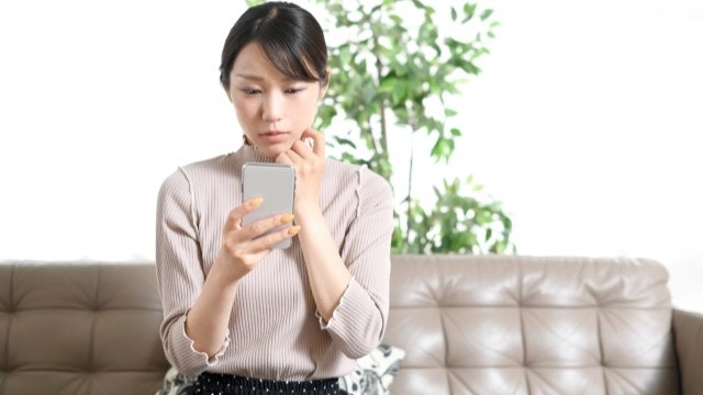 女性が携帯を見ながら悩んでいる様子