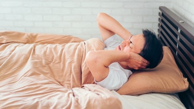 ベッドで耳を塞ぐ男性