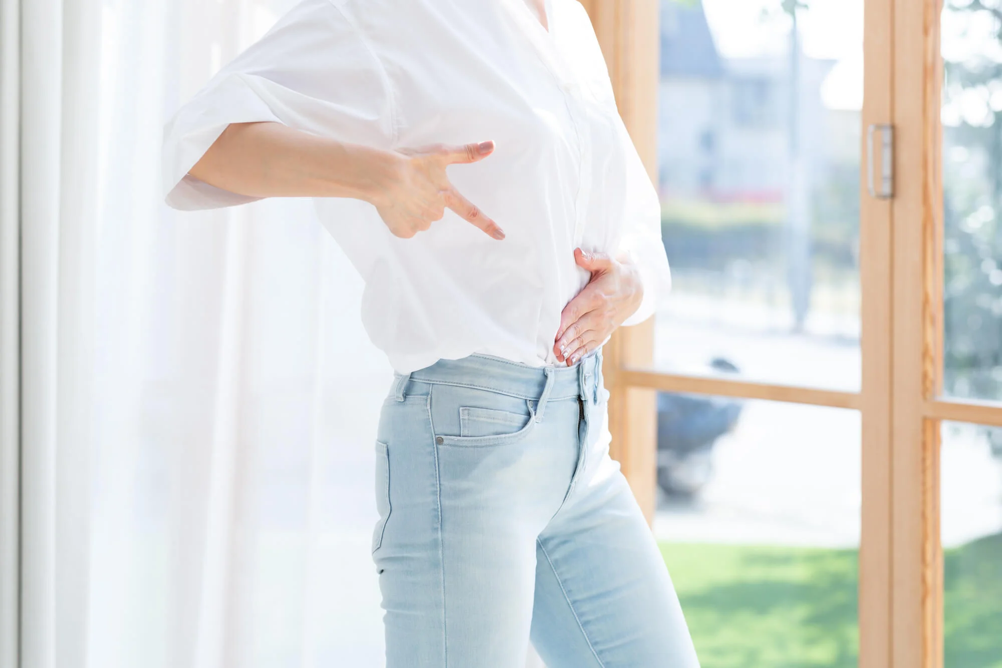 自分の腰の辺りを指さす女性