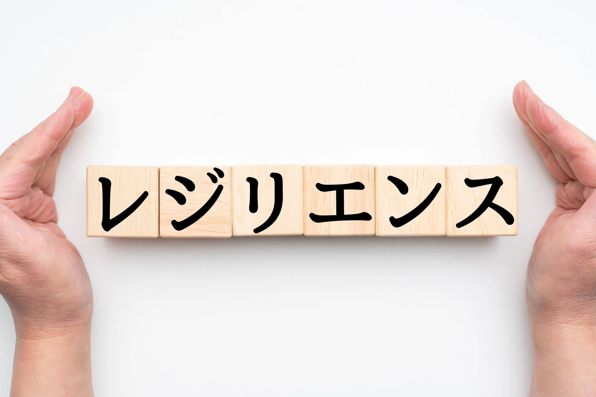 レジリエンスと書かれた積み木と、それを囲うように置かれた両手