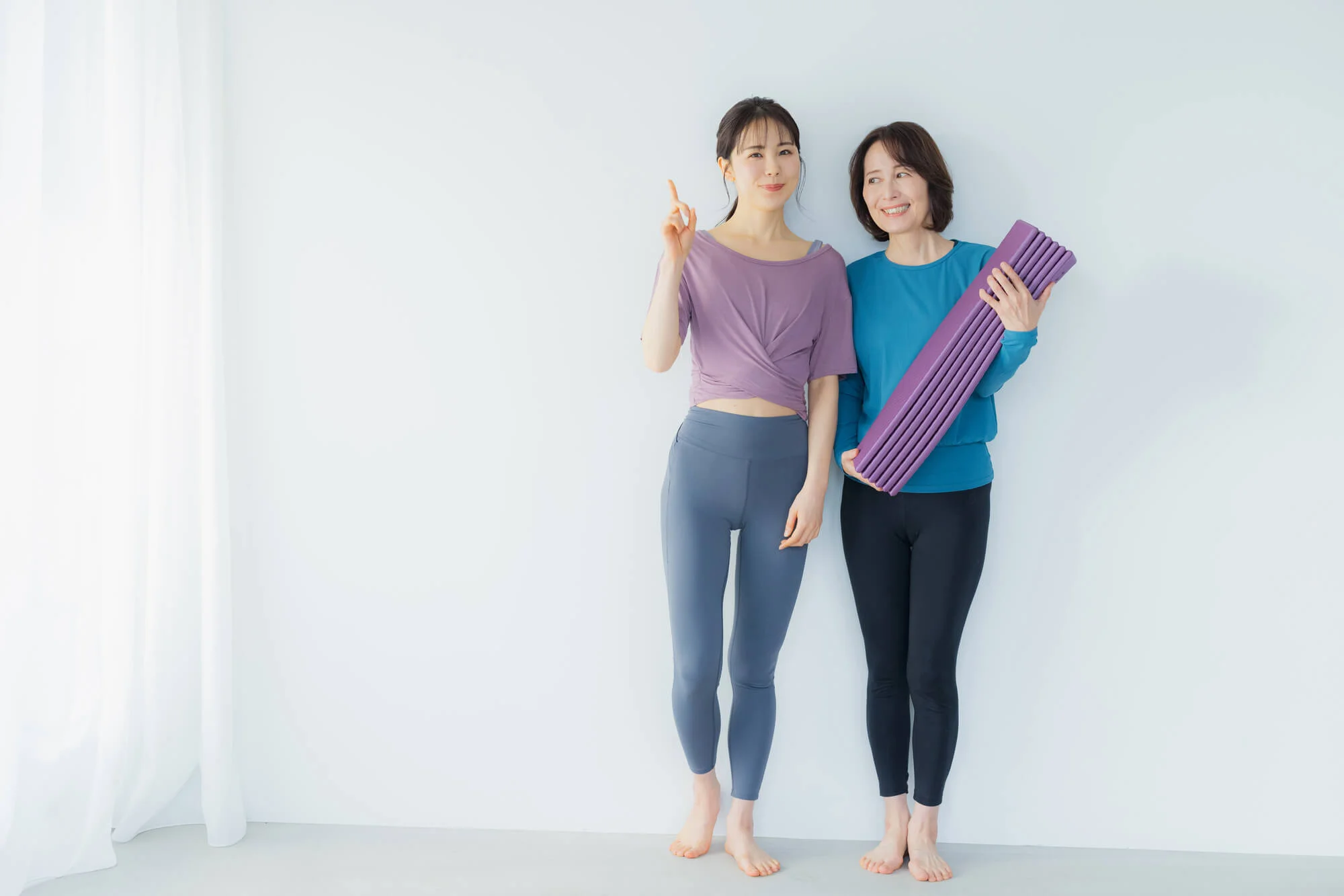 ヨガマットを持つ女性と人さし指を立てる女性