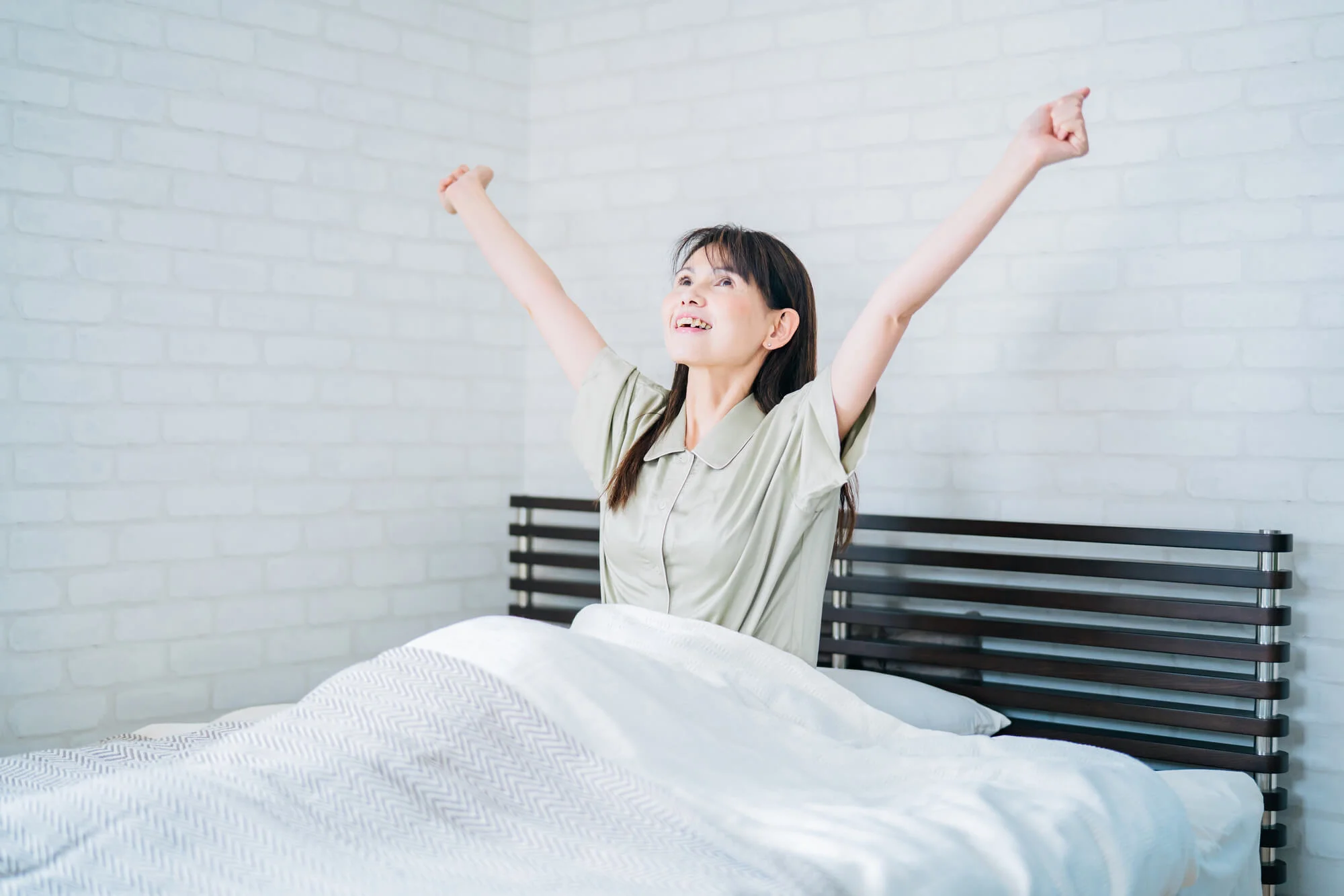 ベッドの上で両手を伸ばし大きく伸びをする女性