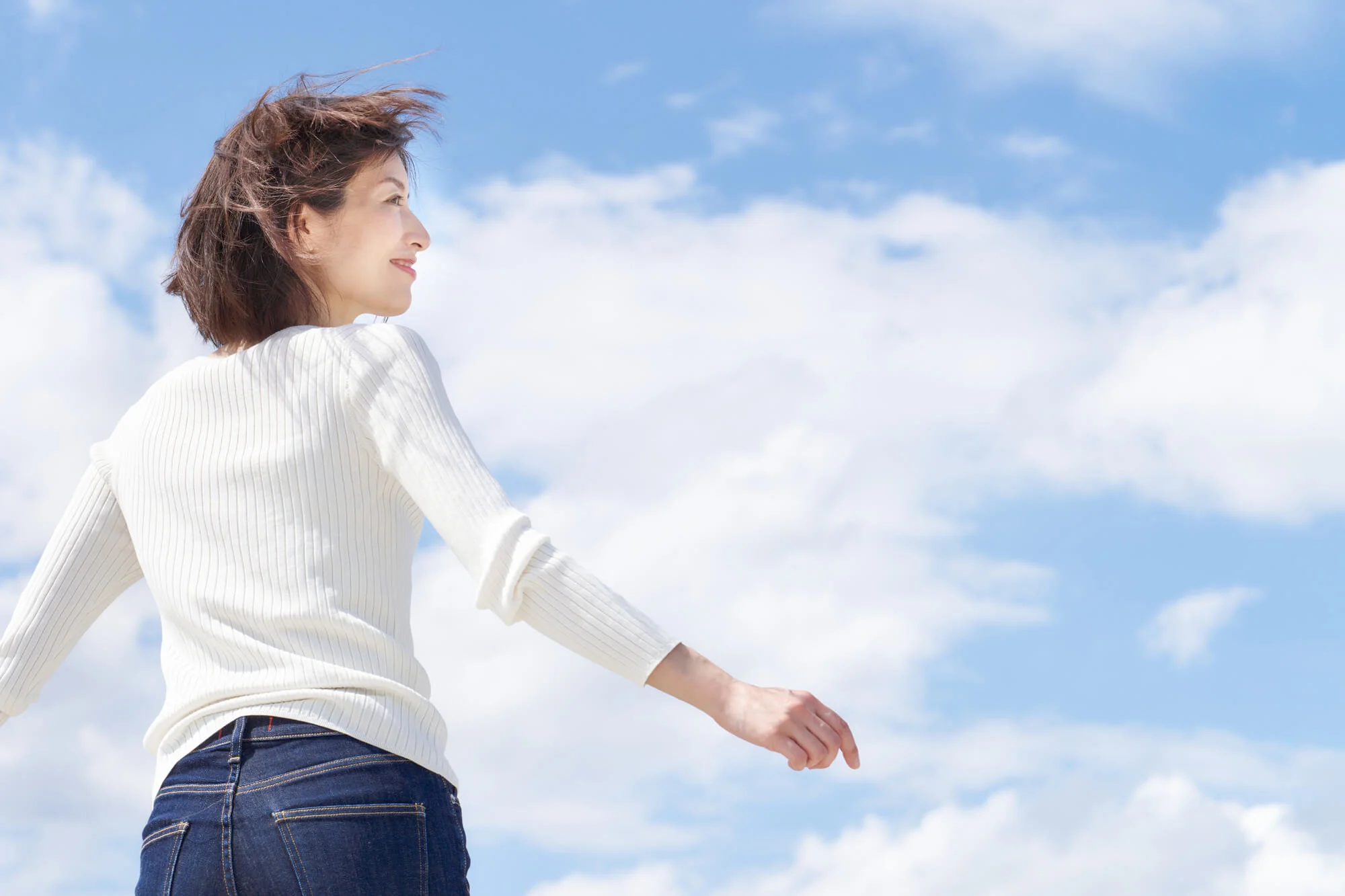 空を背景に腕を広げる女性の後ろ姿