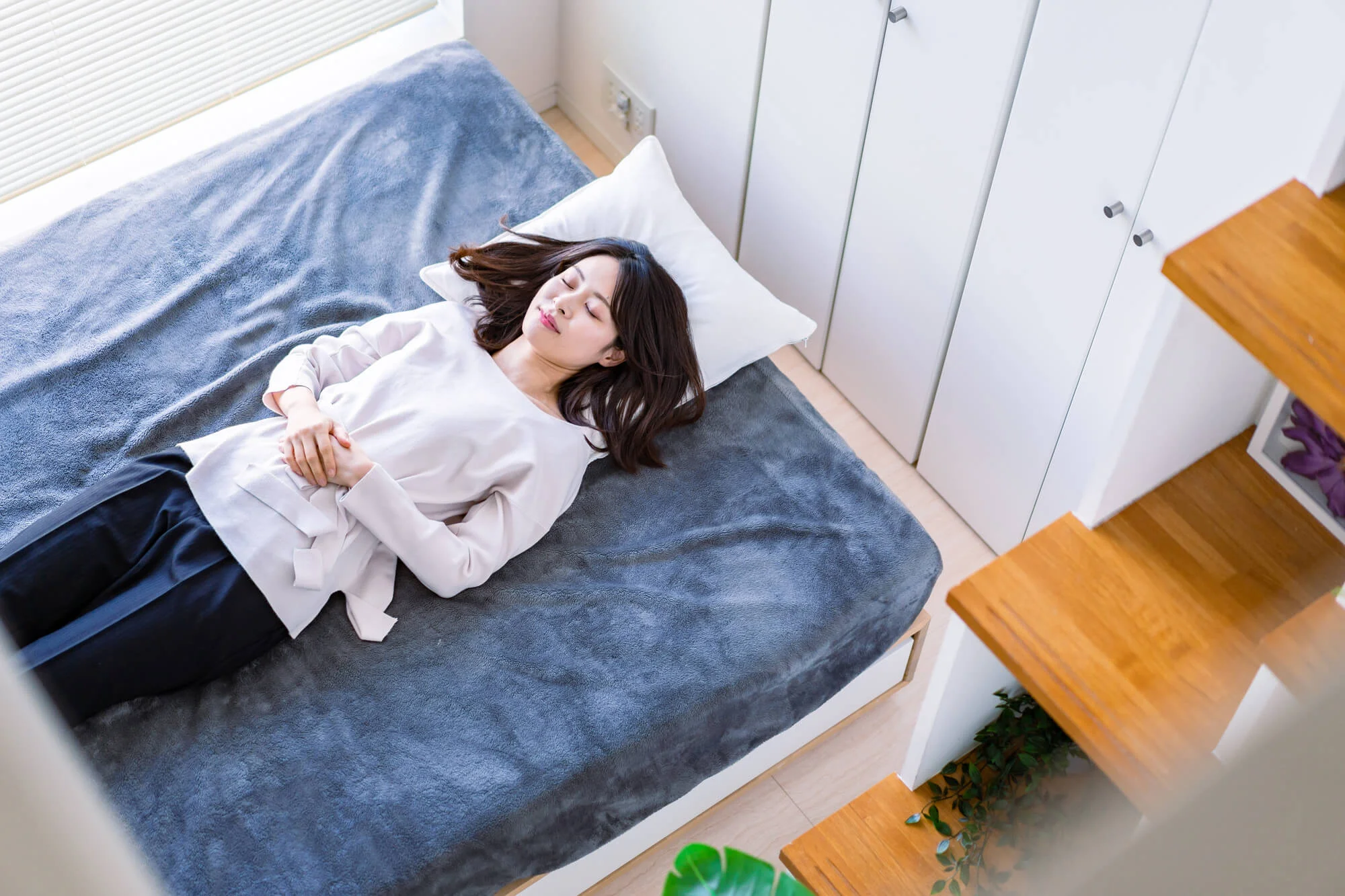 ベッドの上で仰向けになり、目をつむりおなかに両手を置いている女性