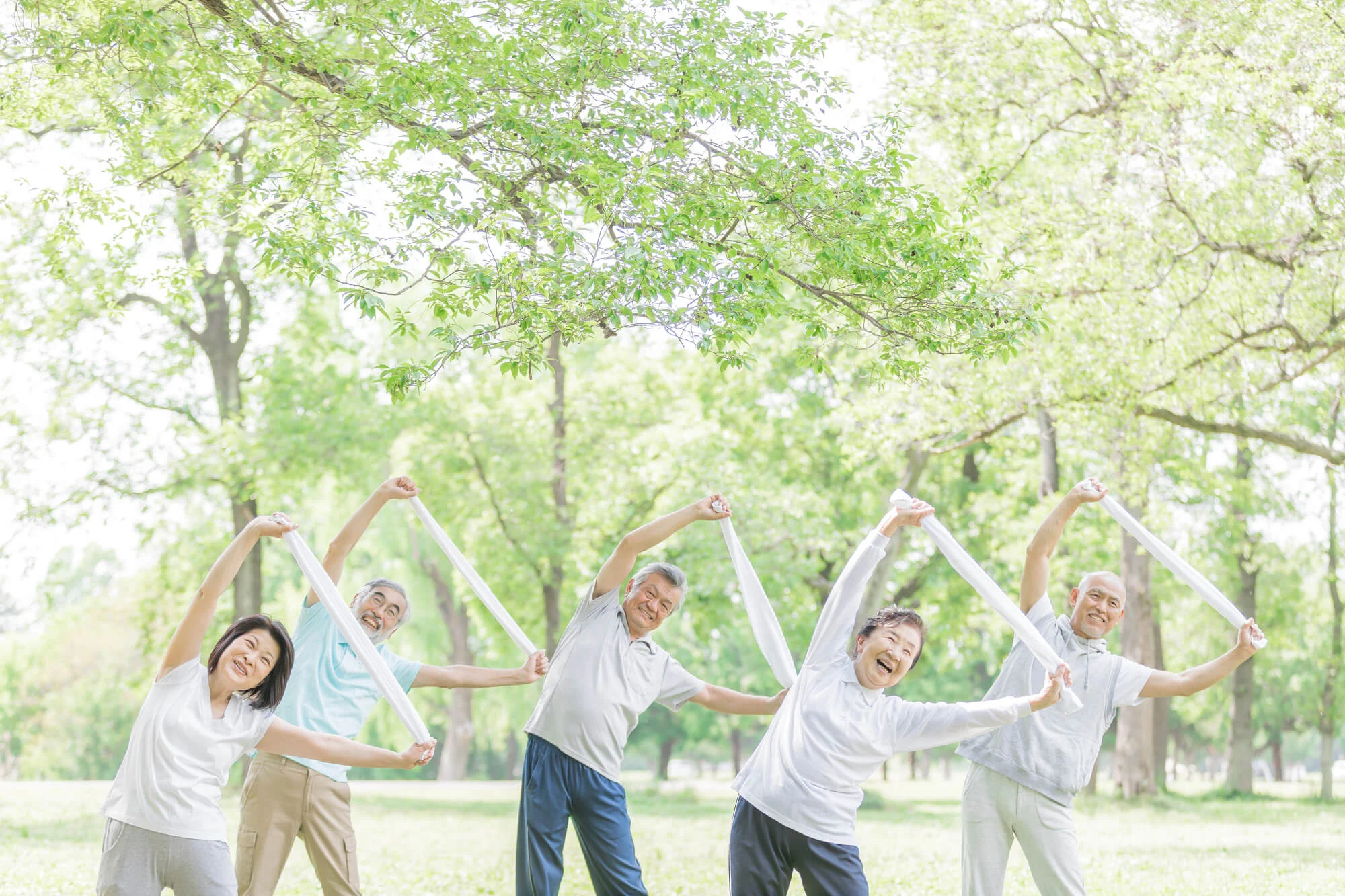 屋外でタオルを使った体操をしているシニアのグループ
