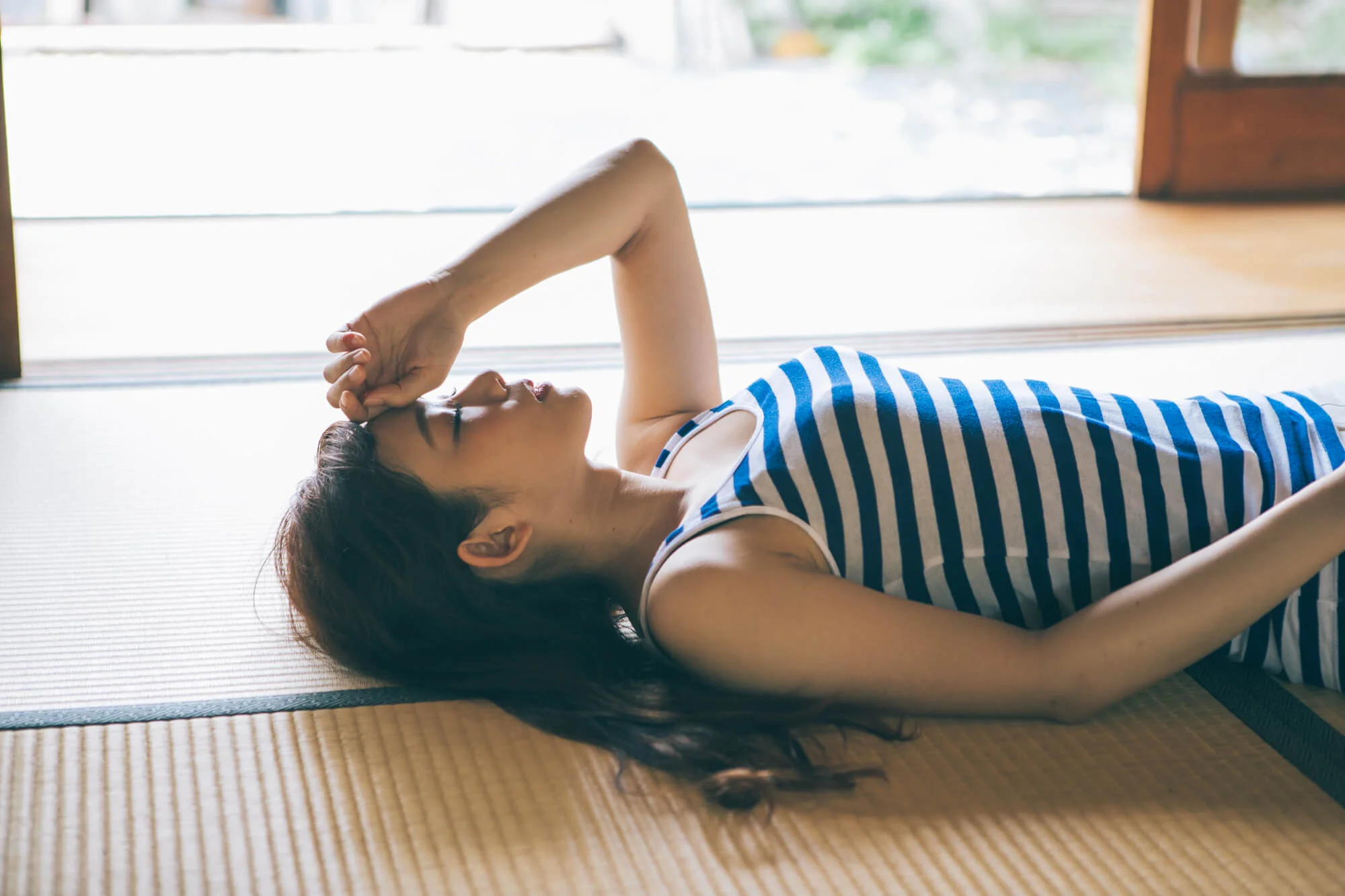 室内の畳の上で、額に手を置き仰向けになる女性