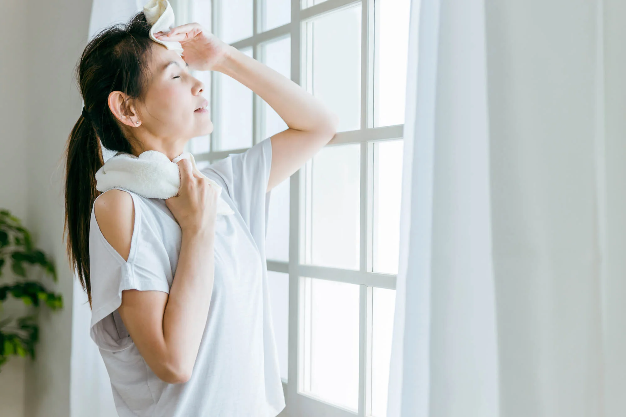 ひたいの汗をタオルで拭う女性<br />