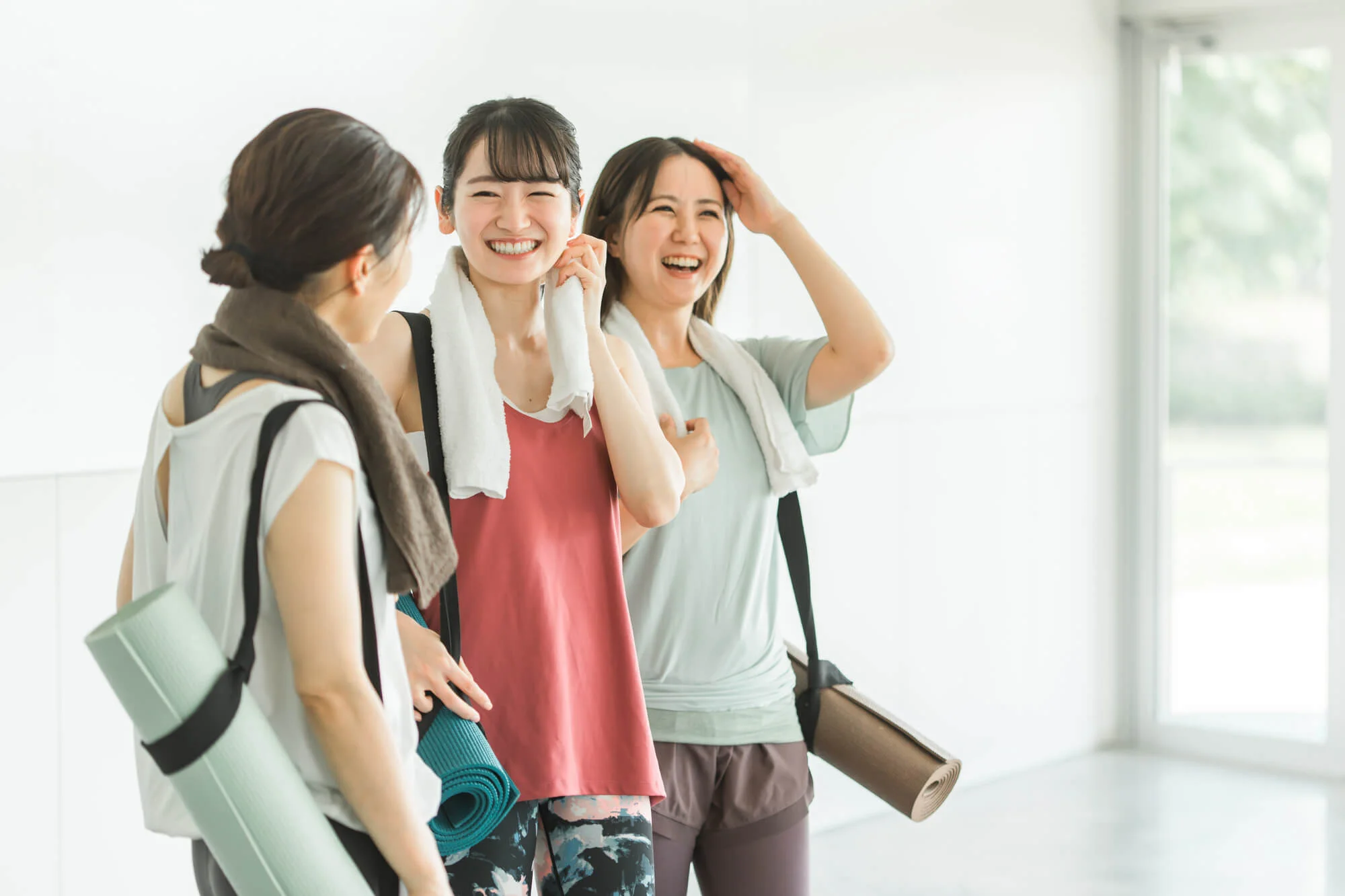 ピラティスマットを持ち、スタジオ内で談笑する3人の女性