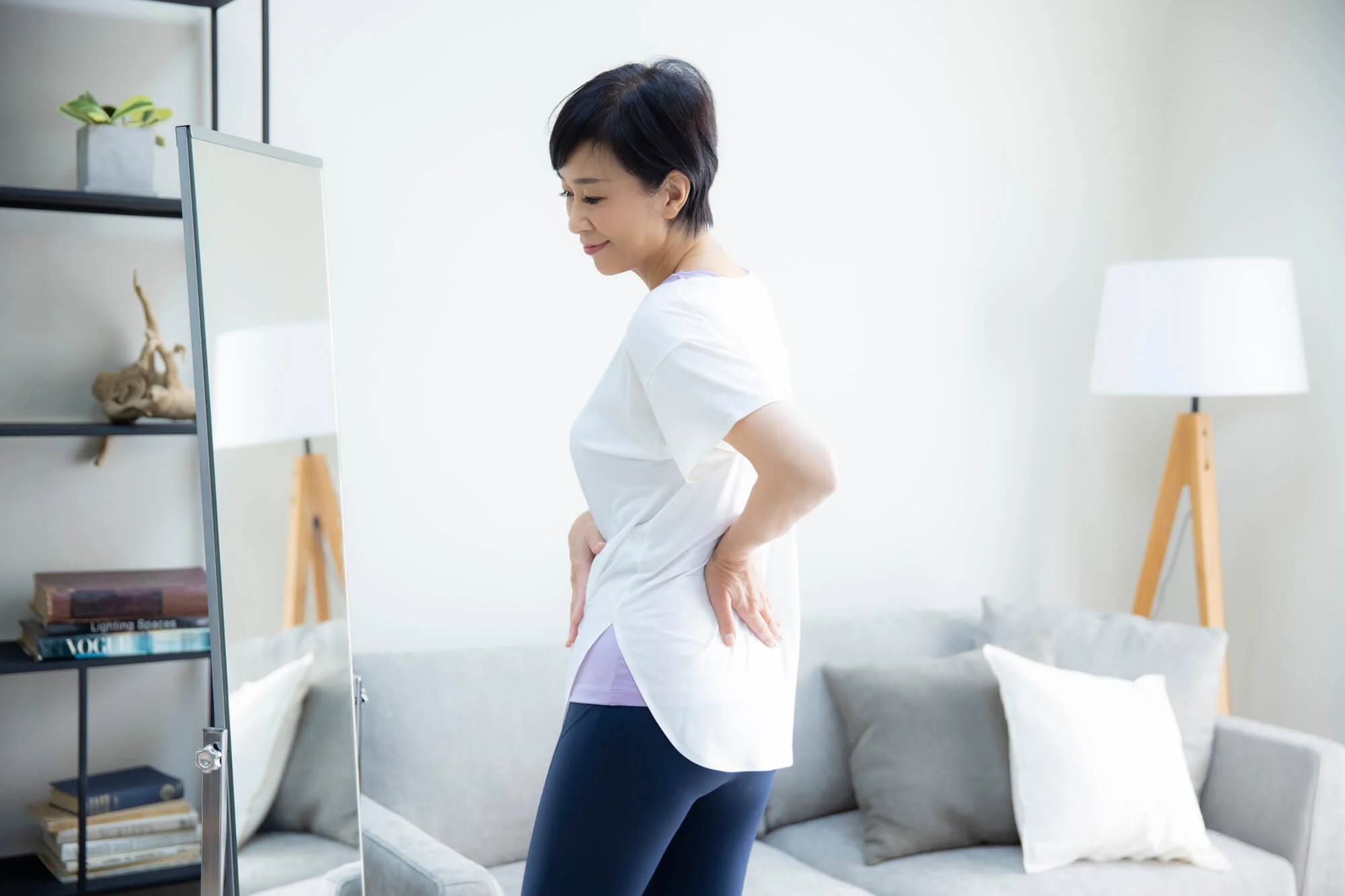 鏡の前で腰とおなかに手を当てる女性