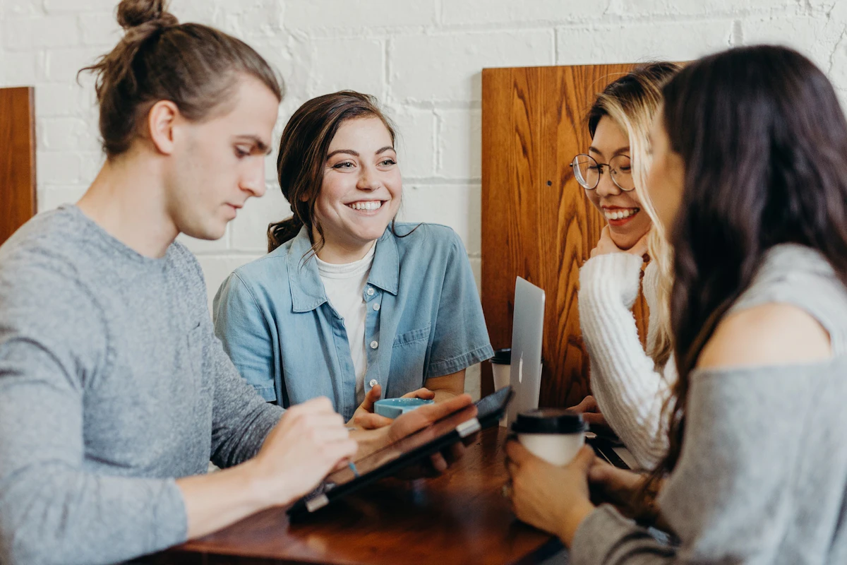 カフェのテーブルでタブレットを囲み、笑顔で話す4人の若者