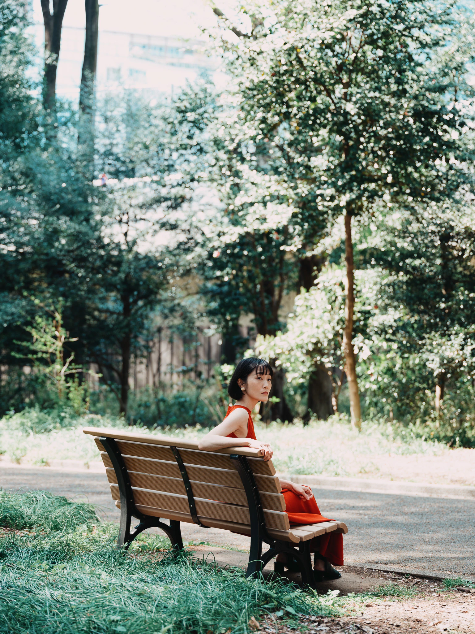 ポートレイト。オレンジのワンピースでショートカット。公園のベンチに座って振り返っている。