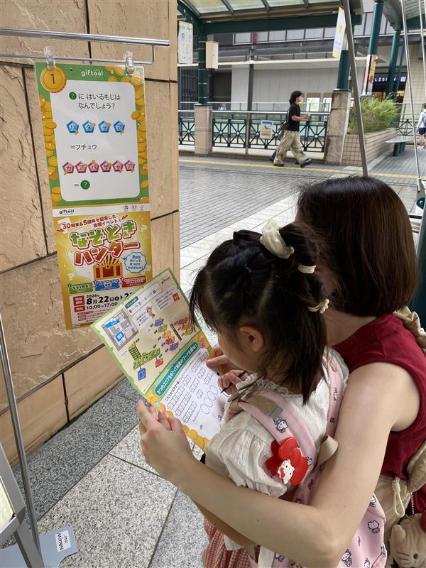 子どもが台紙に向かう様子を同行する大人が見守る場面