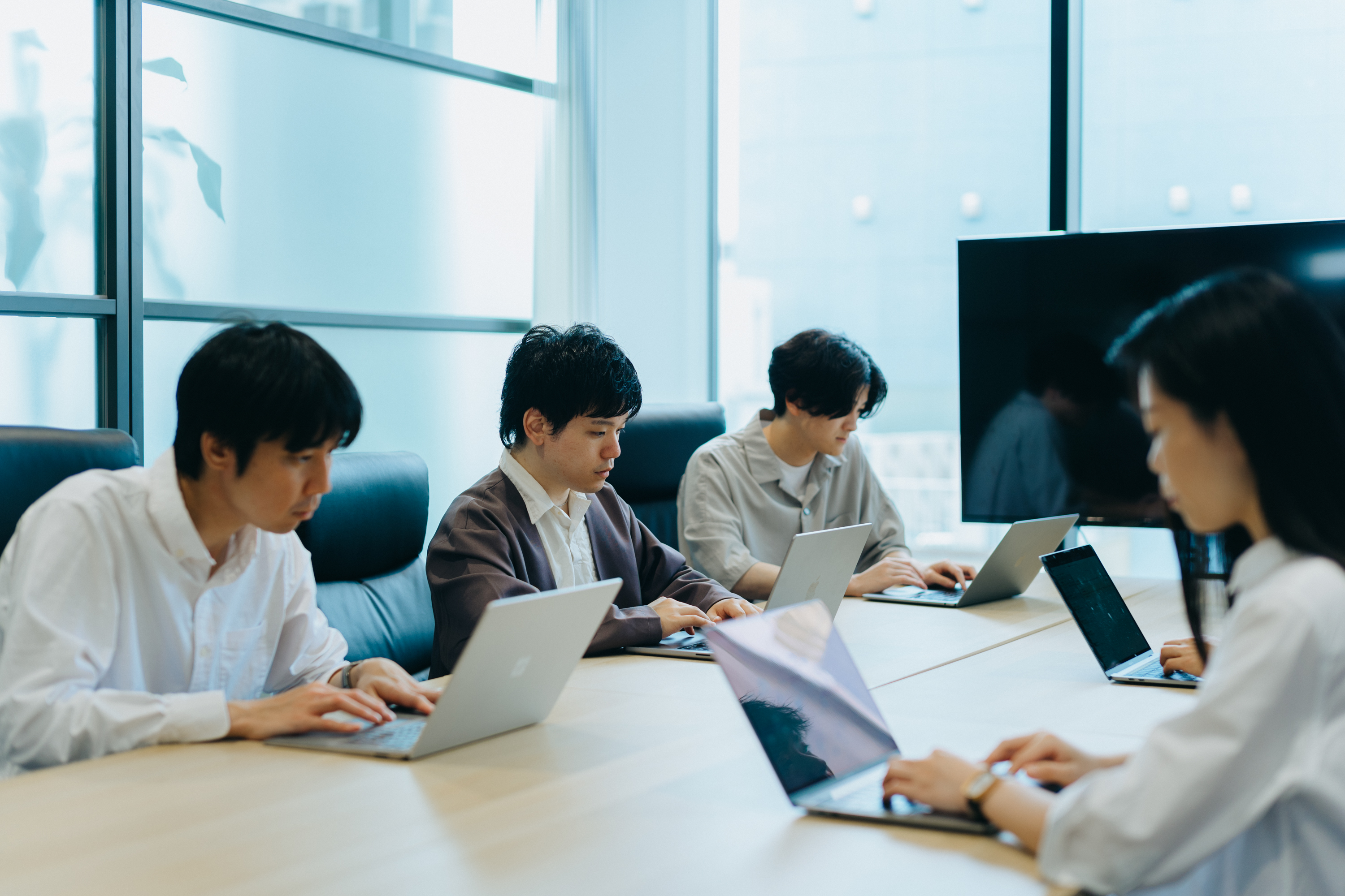 オフィスの会議室の長机で向かい合わせに4名の社員が仕事をしている写真。