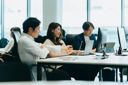 オフィス内の長机に3名の社員が並んで座り話し合いながら作業をしている写真。