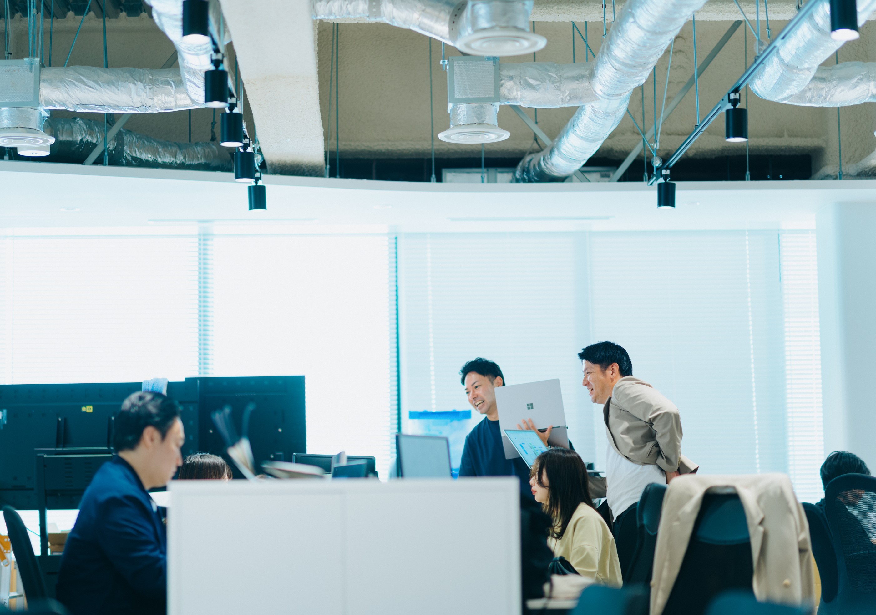 向かい合わせになった長机で作業する1名の社員と3名で相談しながら作業する社員の写真。