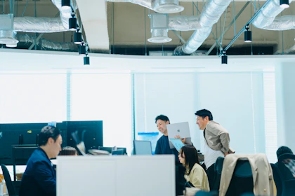 向かい合わせになった長机で作業する1名の社員と3名で相談しながら作業する社員の写真。