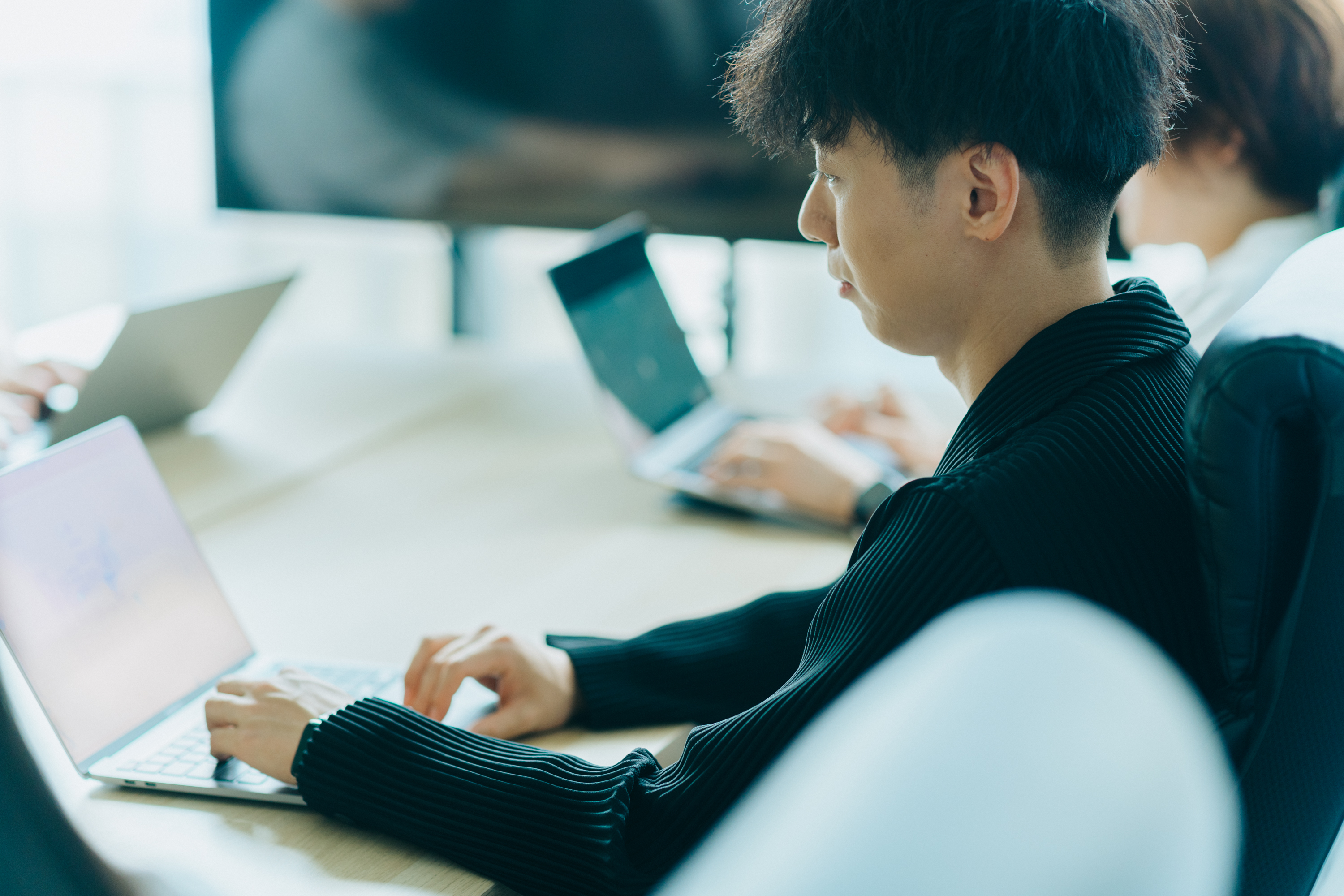 向かい合わせに座っている3名のスタッフが仕事をしている写真。