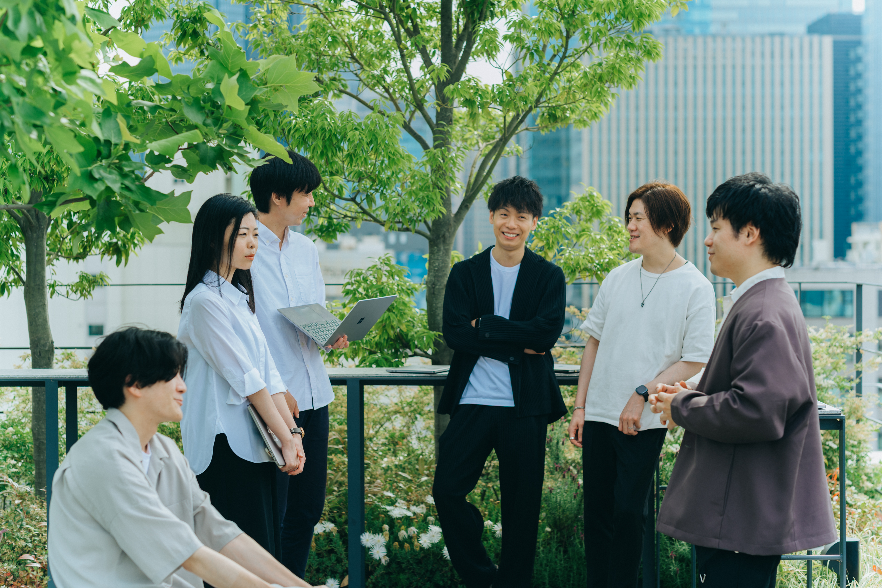 屋上のテラスで6名のスタッフが向かい合わせに立ち、談笑をしている写真。