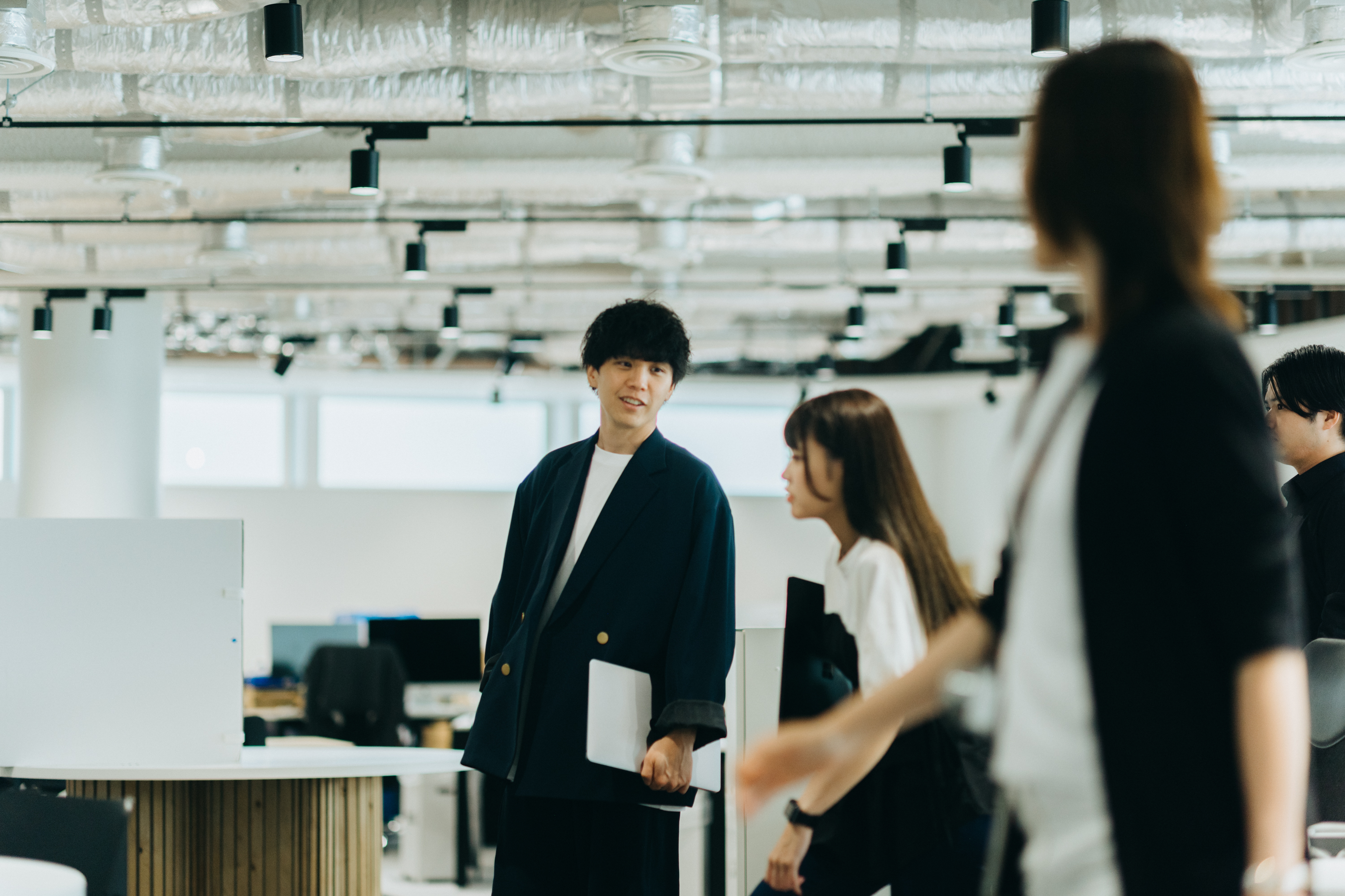 ラップトップパソコンを持った1名の社員と並んで談笑しながら歩く2名の社員の写真。