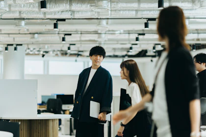 ラップトップパソコンを持った1名の社員と並んで談笑しながら歩く2名の社員の写真。