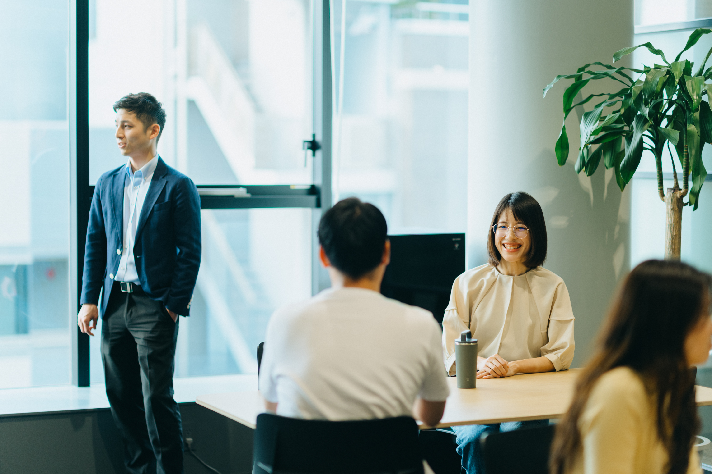 打ち合わせエリアで向かい合って打ち合わせをする1組の社員と他の社員と立ち話をしている1名の社員の写真。