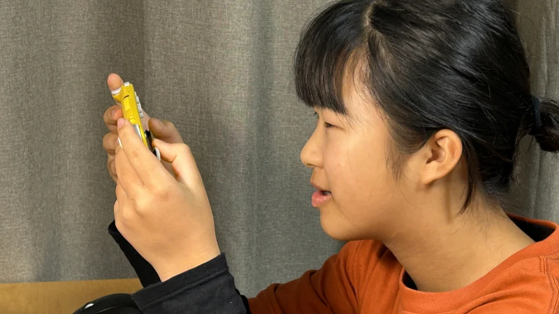 オレンジ色の服を着てポニーテールをした女の子の横顔。手に持った黄色のNintendo Switch Liteの画面を見つめ、穏やかな表情でゲームをプレイしている。