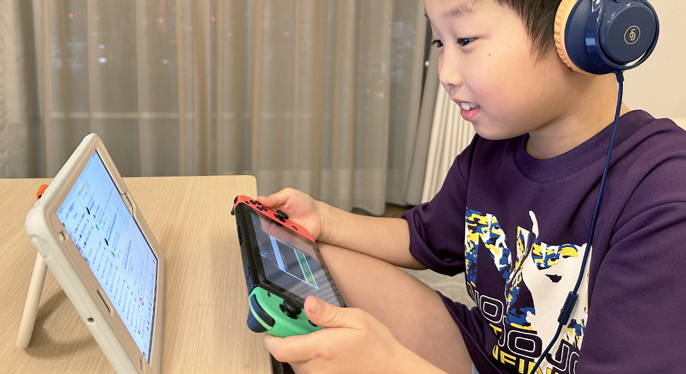 ヘッドフォンをつけ、Nintendo Switchをプレイしながらモニターを見ている男の子