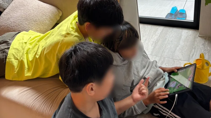 リビングルームのテレビの前に4人の子どもたちが集まり、画面を覗き込むように並んで立っている後ろ姿。