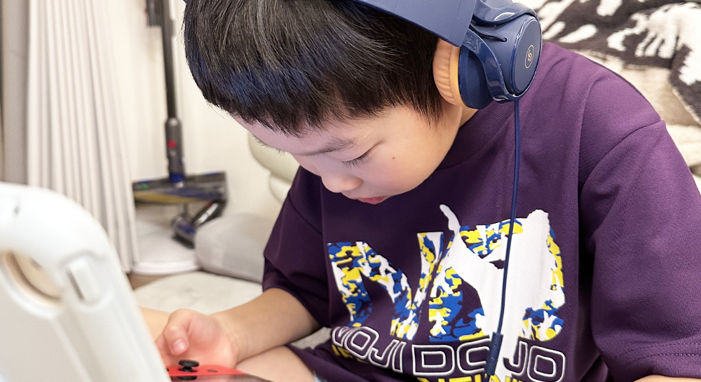 ヘッドフォンをつけ、手に持っているNintendo Switchを覗き込んでいる男の子