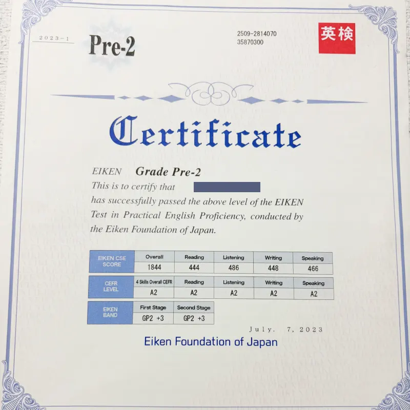実用英語技能検定（英検）の「準2級（Pre-2）」の合格証書（Certificate）の画像。スコアの表が記載されており、氏名部分はプライバシー保護のために青い線で隠されている。