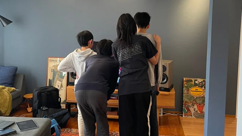 リビングルームのテレビの前に4人の子どもたちが集まり、画面を覗き込むように並んで立っている後ろ姿。