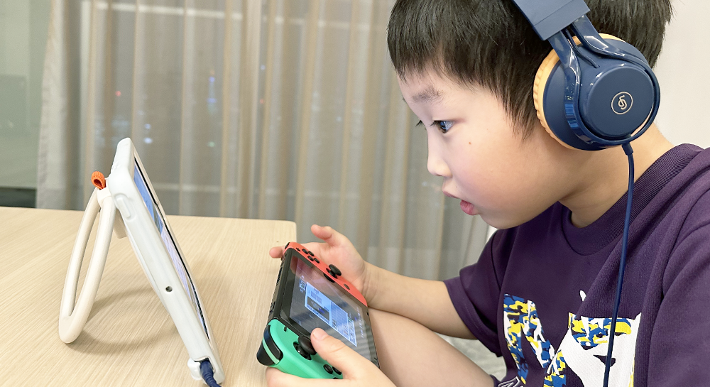 ヘッドフォンをつけ、Nintendo Switchをプレイしながらモニターを見ている男の子