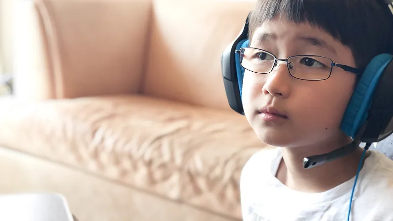 ゲーミングヘッドセットを装着した、眼鏡をかけた男の子の顔のクローズアップ。口元まで伸びたマイクを付け、少し上を見つめる真剣な表情から、ゲームやコミュニケーションに深く集中している様子が伝わる。