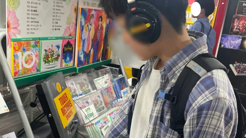 CDショップの試聴機の前で、ヘッドホンをつけて音楽を聴いているチェック柄のシャツを着た男の子。