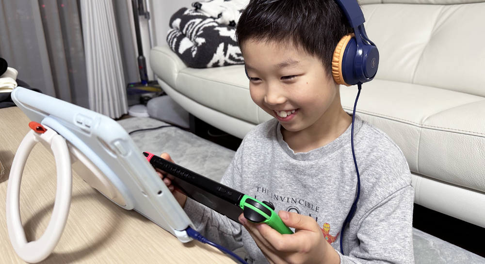 ヘッドフォンをつけ、Nintendo Switchをプレイしながらモニターを見ている男の子