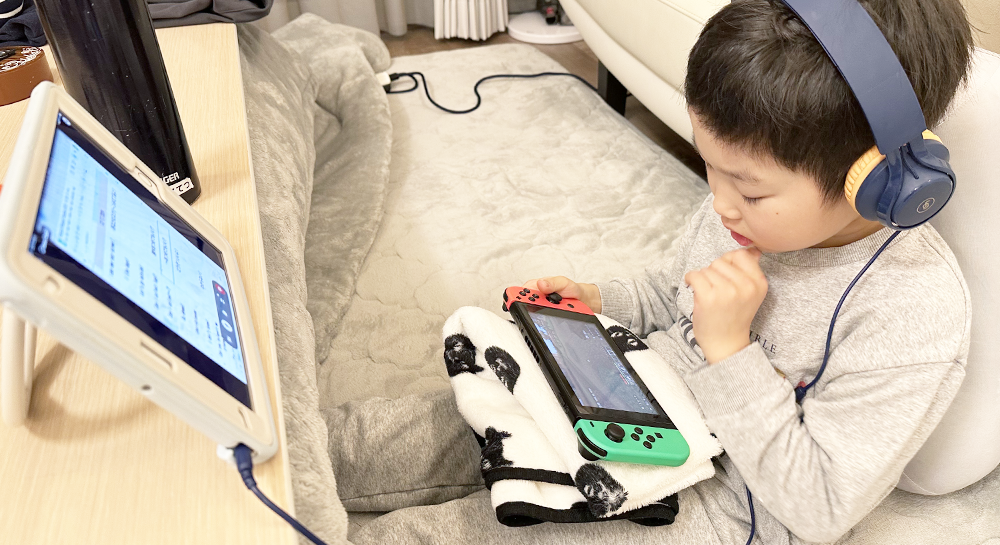 ヘッドフォンをつけ、手に持っているNintendo Switchを覗き込んでいる男の子