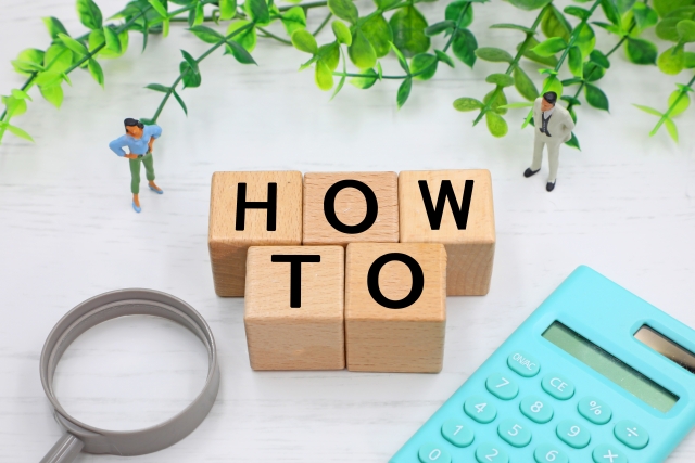 「HOWTO」の文字ブロックと虫めがねと電卓