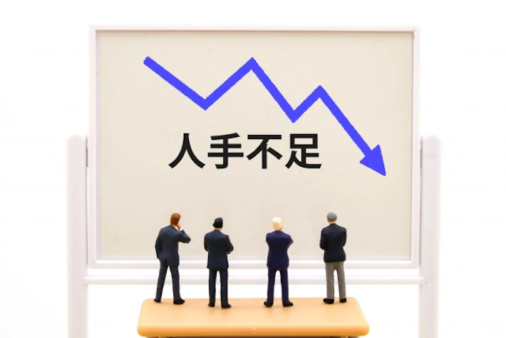 「人材不足」と書かれたホワイトボードを見る会社員