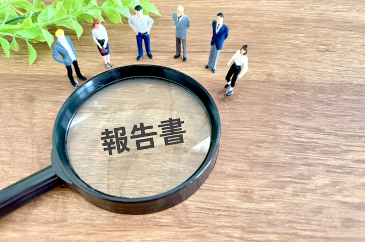 「報告書」と書かれた虫めがねを見る会社員