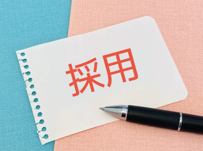 「採用」の文字が書かれた紙とペン
