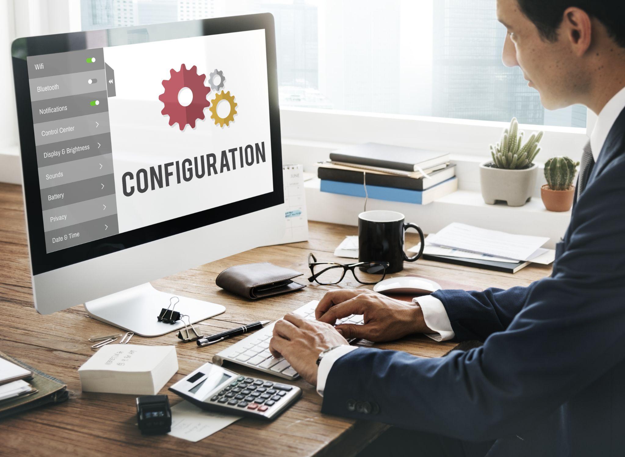 デスクトップPCの画面に「CONFIGURATION（設定）」と表示され、ビジネスパーソンがキーボードを操作している様子