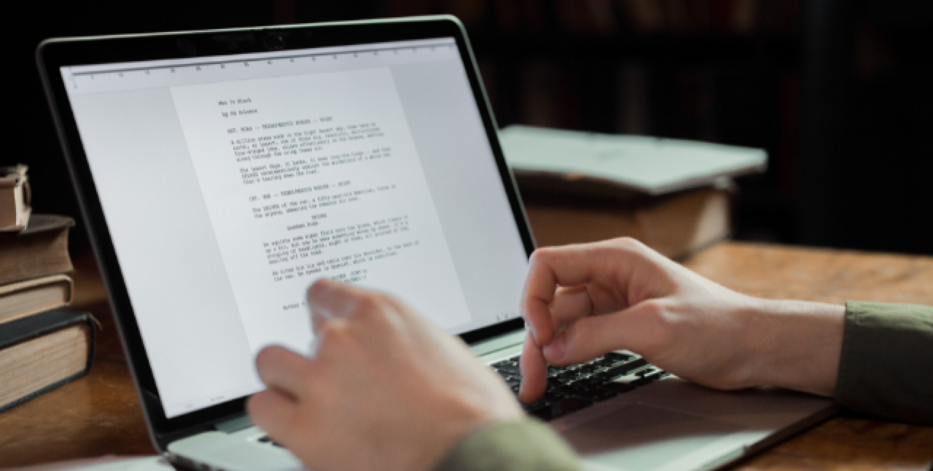 木製のデスクでノートパソコンを開き、キーボードを打って文書を作成している様子のイメージ