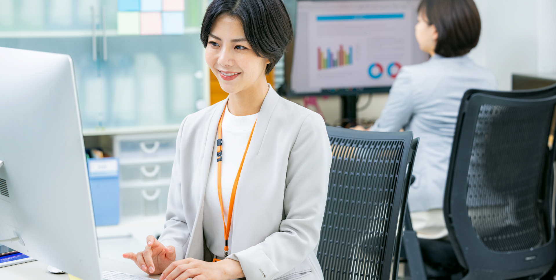 明るいオフィスで、笑顔でデスクトップパソコンに向かって業務を行っている女性の様子