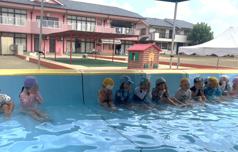 幼稚園のプールに入り、顔に水をかける年少さん