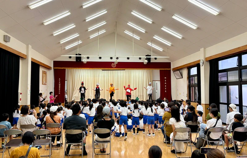 全園児がホールに集まり、先生が舞台の上で誕生会の劇を行っている様子を保護者の方々が楽しそうに見ている様子